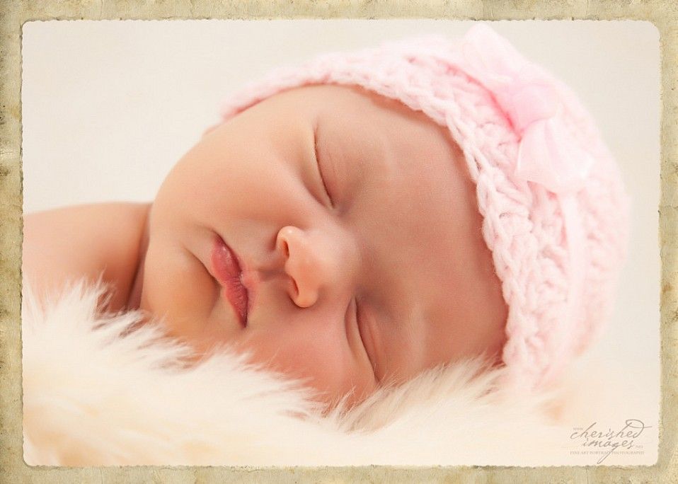 newborn baby with pink hat on white fur