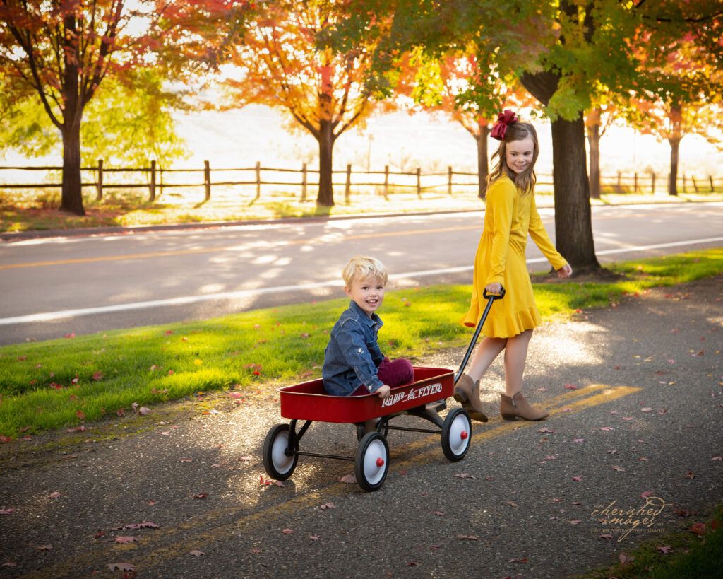 Girl in fall leaves pulling boy in wagon